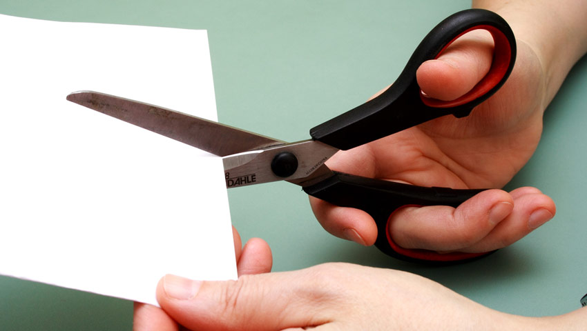 Канцелярские ножницы в руке, разрезающие бумагу